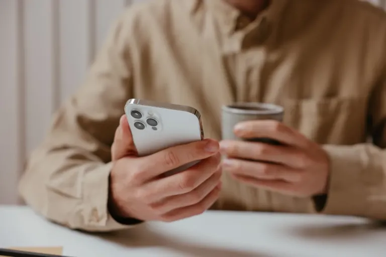 Iemand houdt een iPhone vast aan tafel met een kop koffie ernaast