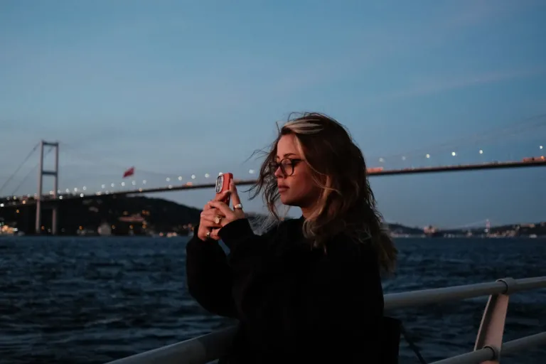 Vrouw maakt met haar telefoon een foto bij de Bosporus in Istanbul, met de Bosporusbrug op de achtergrond