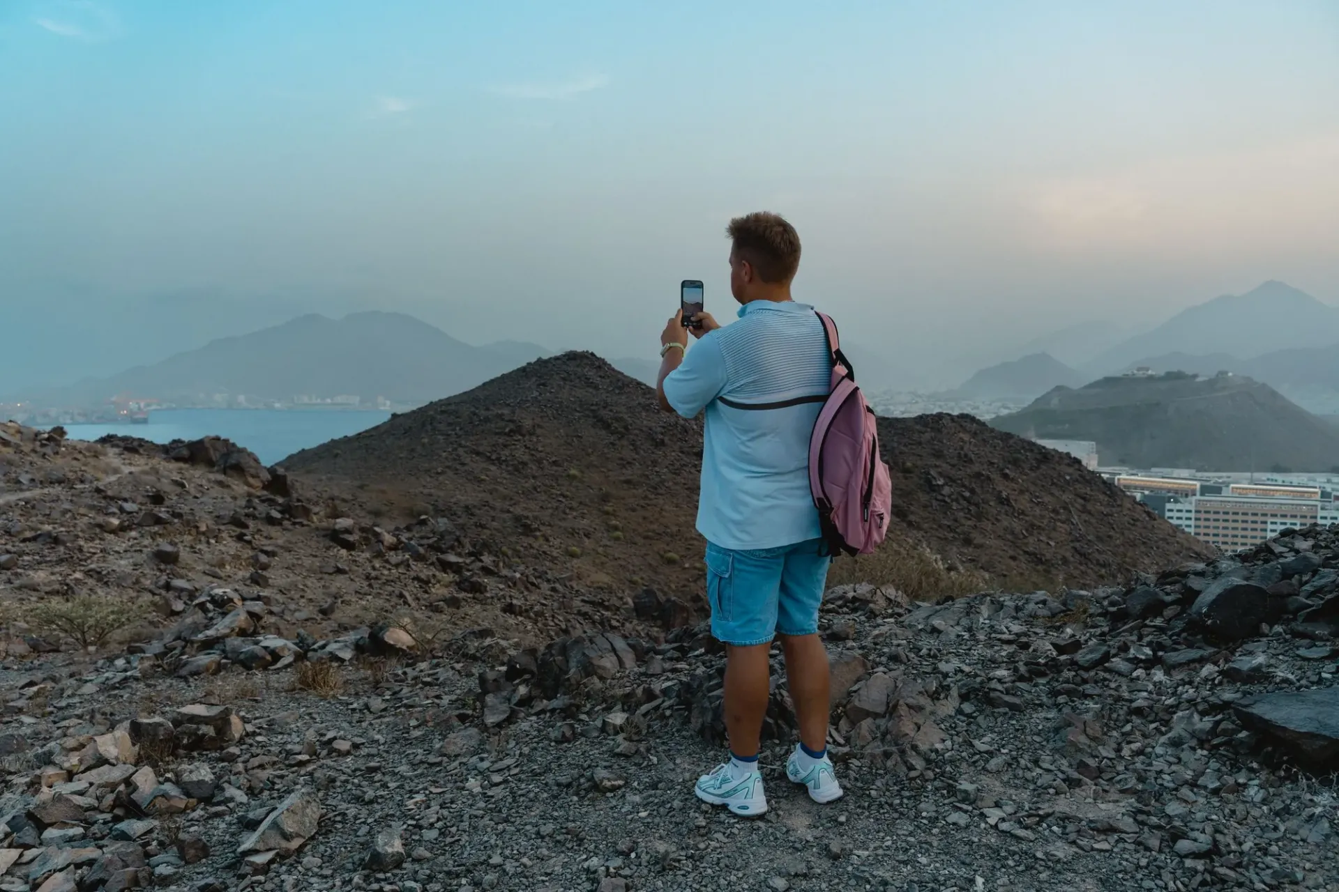 Reiziger met rugzak maakt met zijn smartphone een foto van een berglandschap aan zee