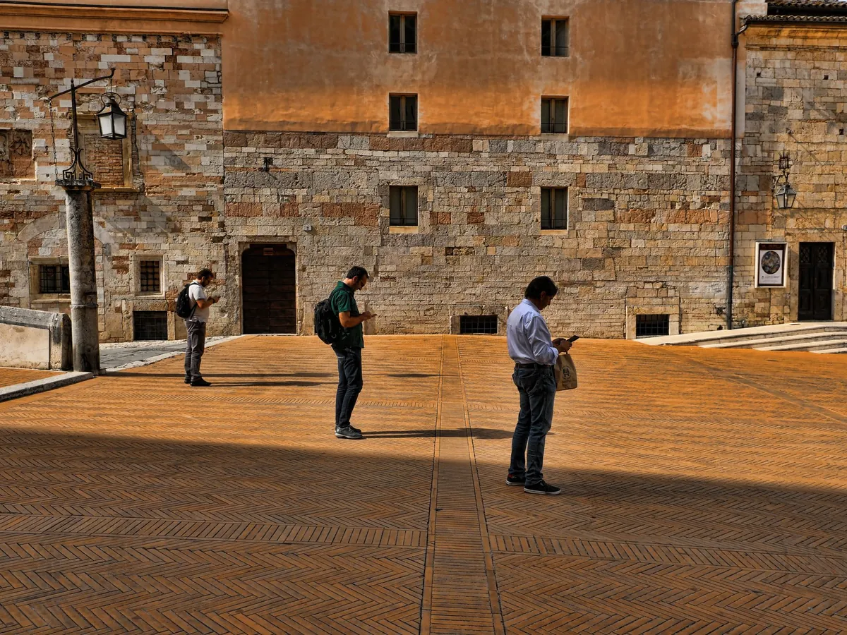 Drie toeristen kijken op hun telefoon op een historisch plein in Italië